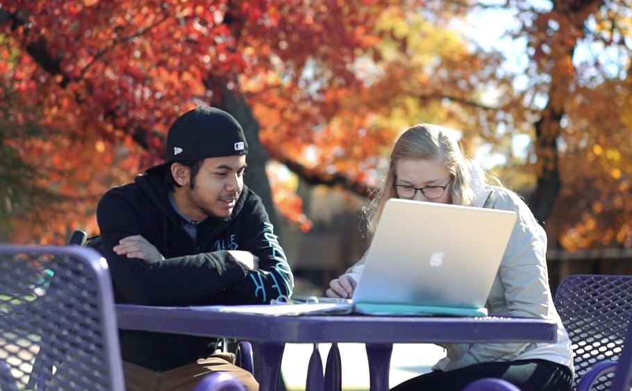Two students sitting at a table outside on campus with a laptop studying