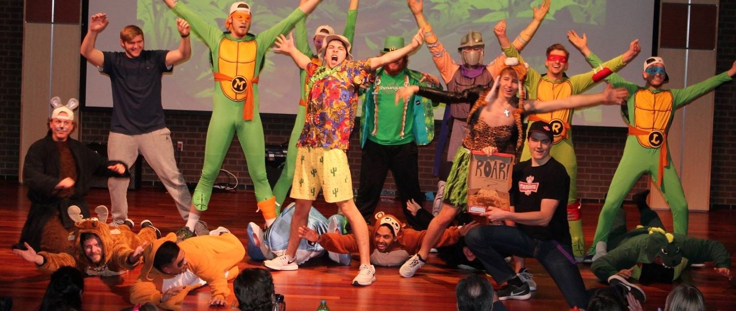 Picture of Fraternity event Wearing Teenage Mutant Ninja Turtles Costumes on stage with their hands in the air