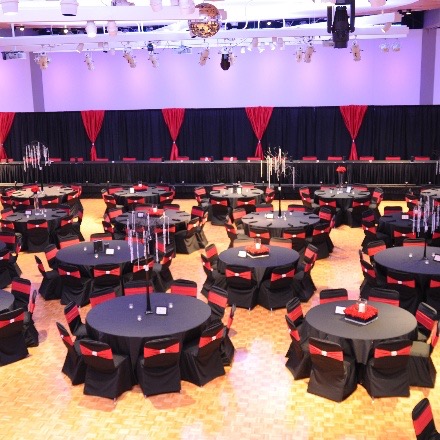Open ballroom with tables and chairs decorated in black and red covers with head table up front. 