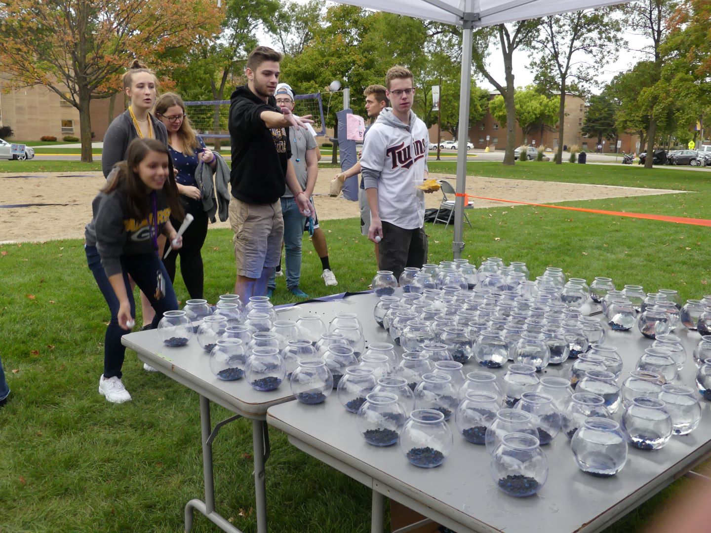 students playing a game of trying to throw a ping-pong ball into a glass vase