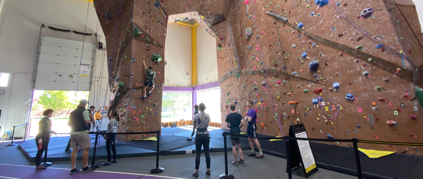 Students waiting to climb the rock climbing wall with instructors