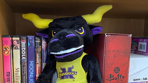 Stomper stuffed toy sitting on a bookshelf