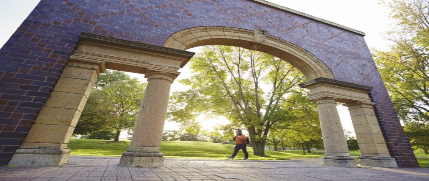 Student outdoors walking under MSU, Mankato campus archway