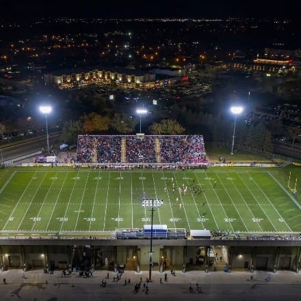 Football field at night with bleachers full of spectators. 