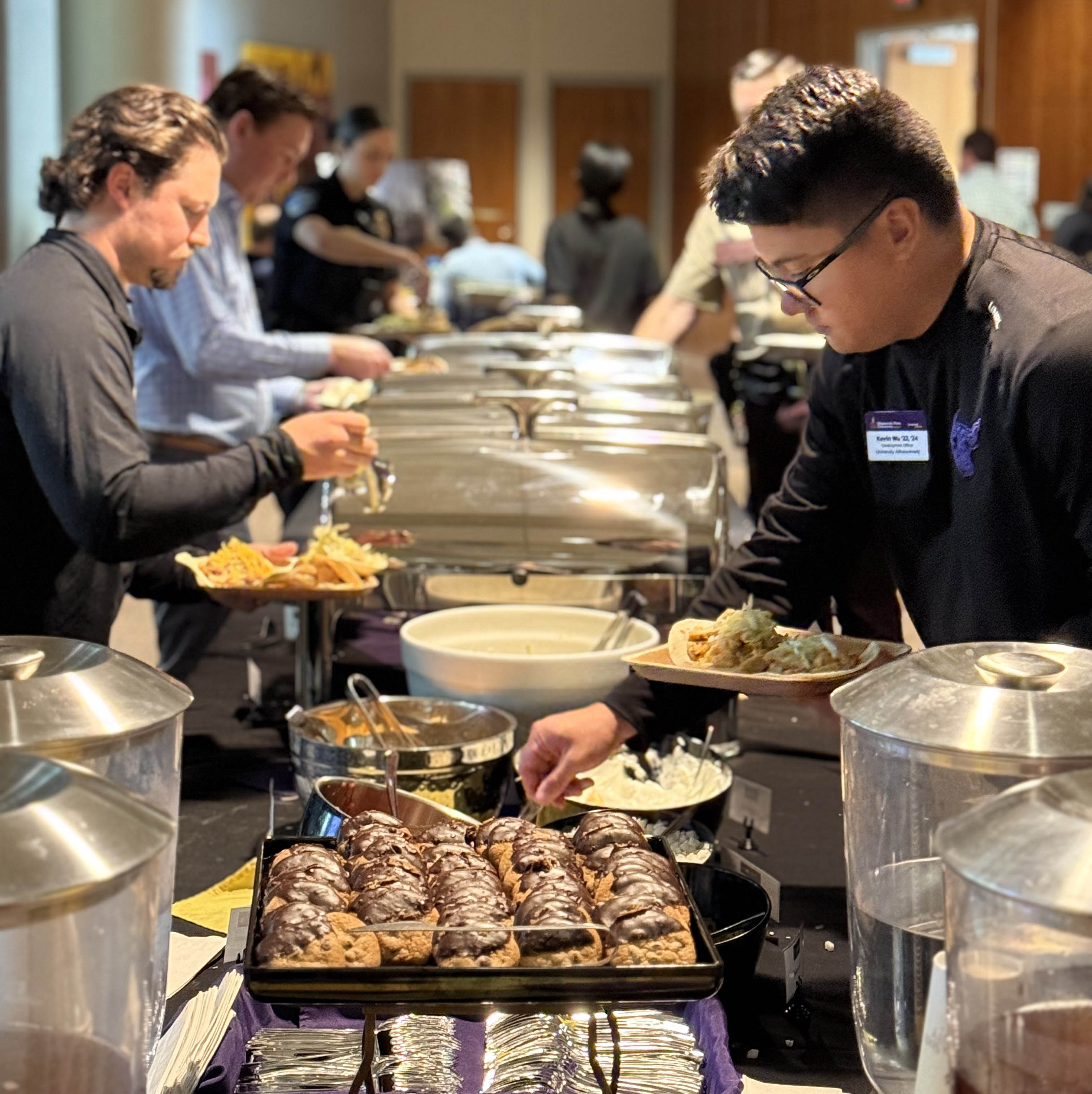 People attending a conference going through the buffet line showcasing dessert and the main dish