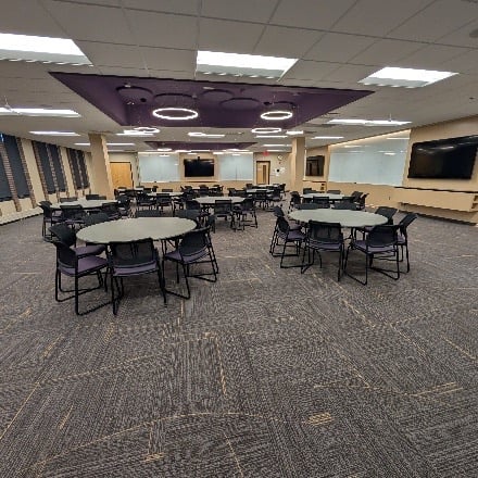 Room with table and chairs and monitors and whiteboards around the room along the walls. 