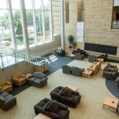 Open space with chairs and a fireplace in the stone wall with large glass windows.
