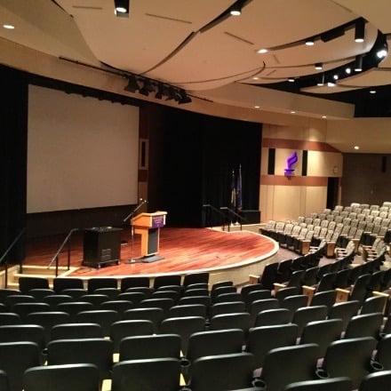 Auditorium with lit stage and chairs.