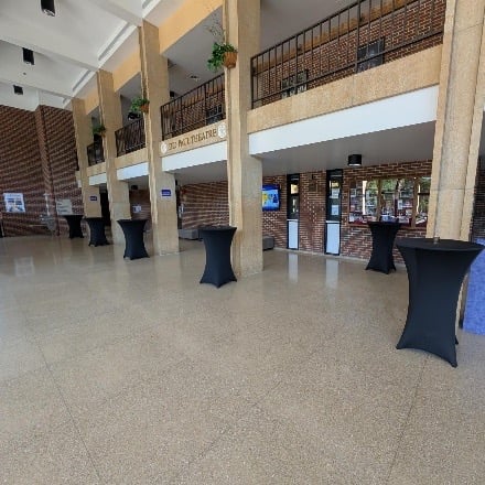 Open lobby with space, pillars, and small high tables with black table cloths.