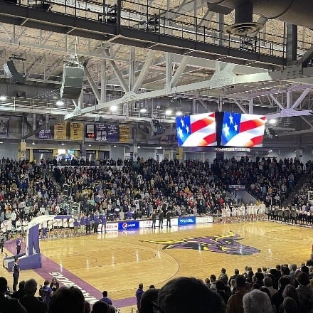 Basketball court with MSU Maverick on center court with a full crowd in the stands. 