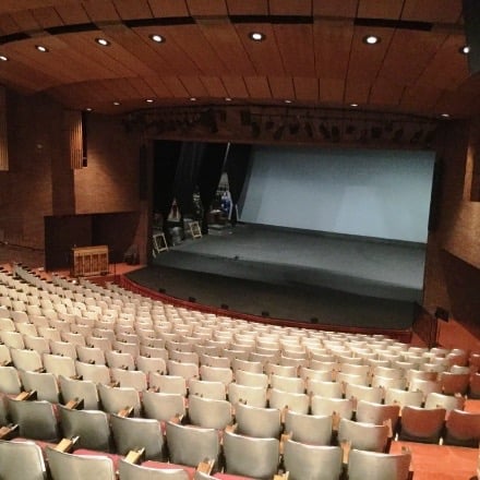 Large theatre stage with lighting front and center with theatre seating rising towards the back.