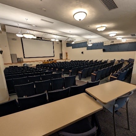 Auditorium with whiteboard in the front of the room and the chairs filling the space behind. 