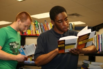 Two students standing in the library reading a book