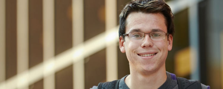 A young man with glasses smiles at the camera.
