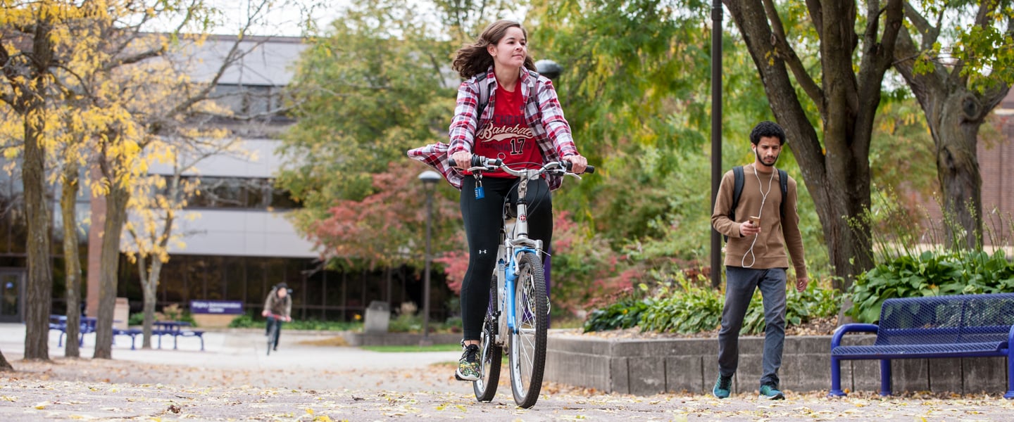 2 students biking in front of the wigleey administration building during the fall season