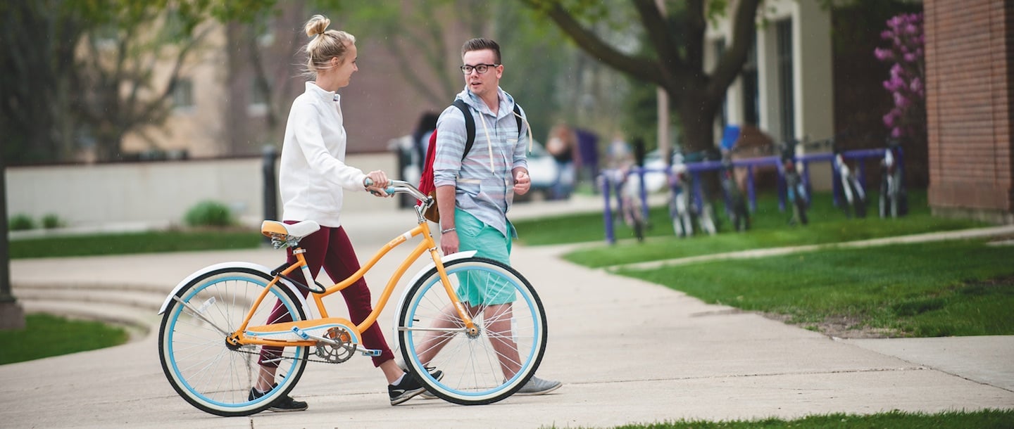 A girl walking her bicycle and talking to a boy outside of Memorial Library