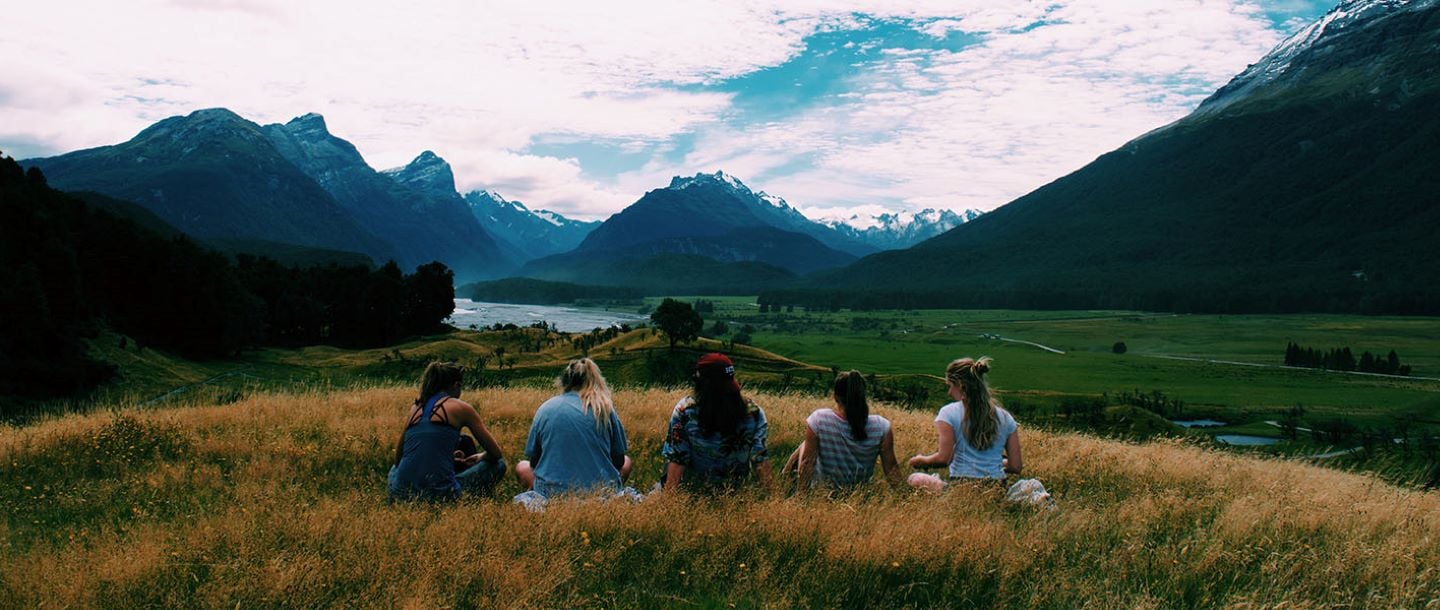Students sitting in a field overlooking a riverbed and mountains