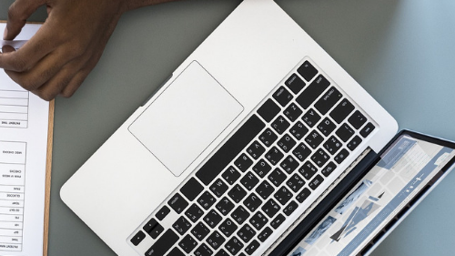 Laptop next to a notebook and person's hand