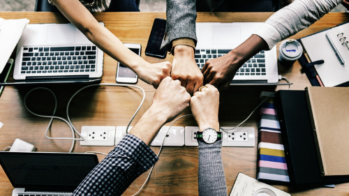 A group of faculty members at a table with their fists united in team work