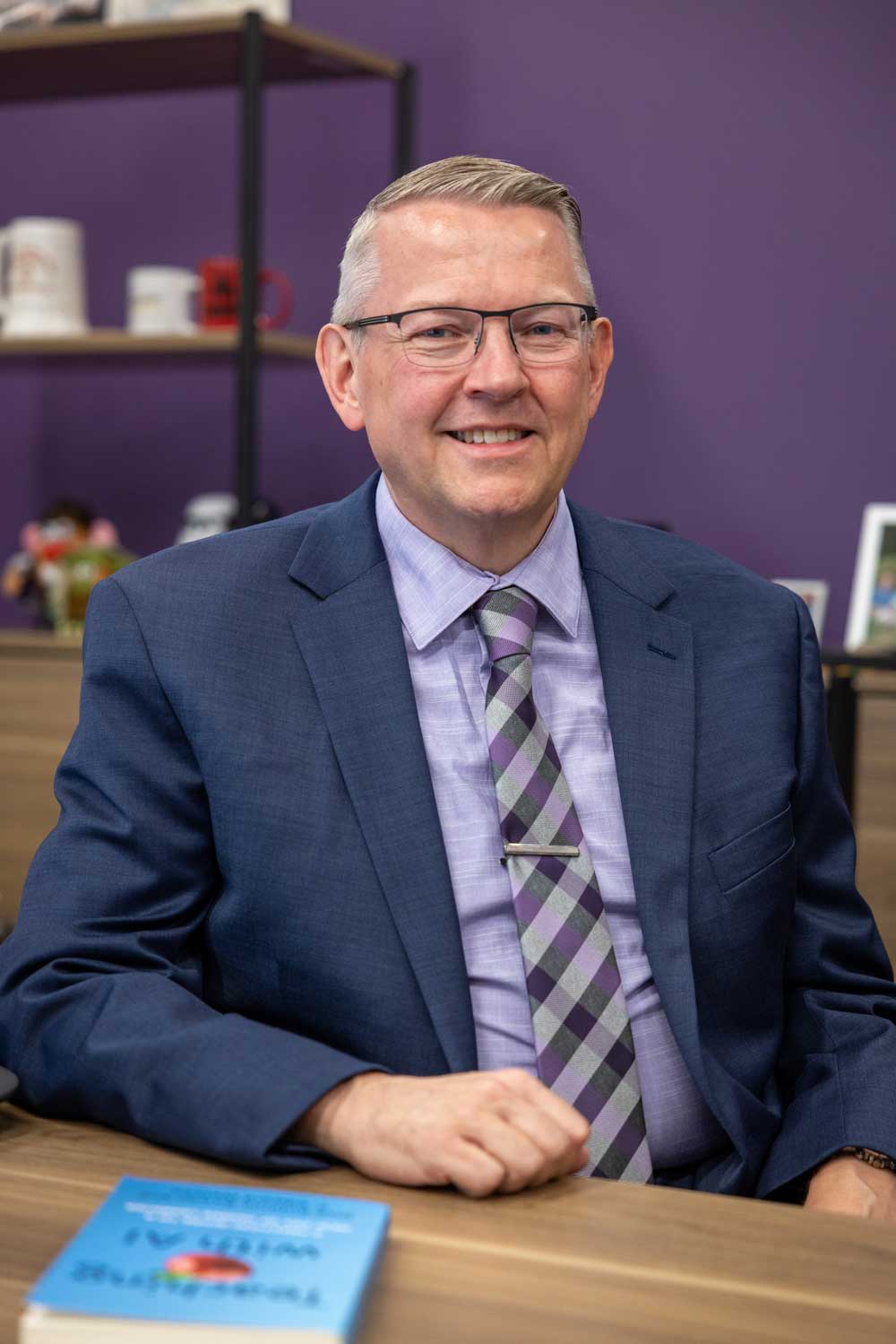 Photo of Joe Kmiech sitting at his desk and smiling at the camera