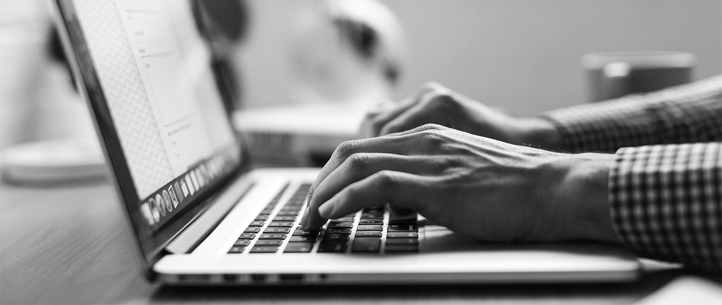 Black and white image of a person's hands typing on a laptop
