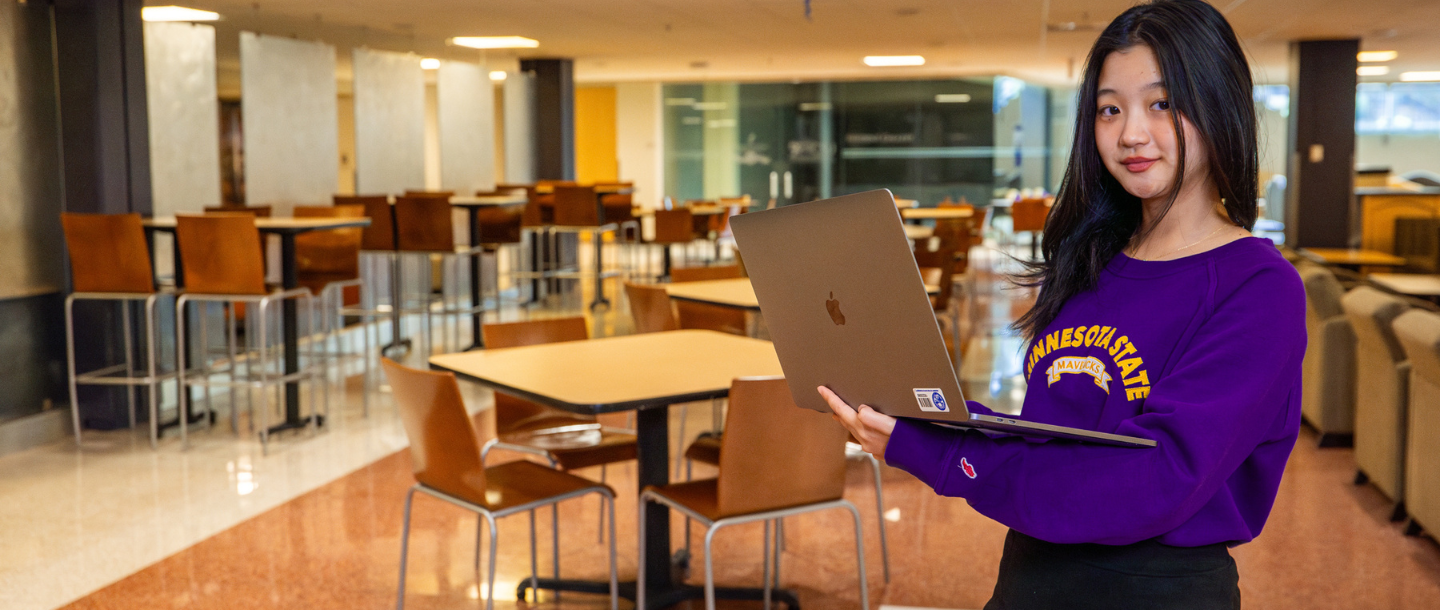 A student holding a laptop in the Centennial Student Union