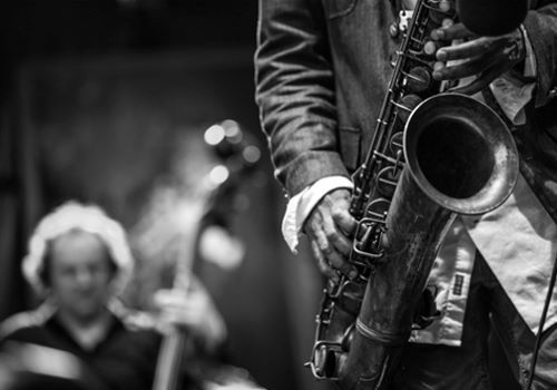 A musical jazz group with close up of someone playing the saxophone and someone playing an upright bass in the background