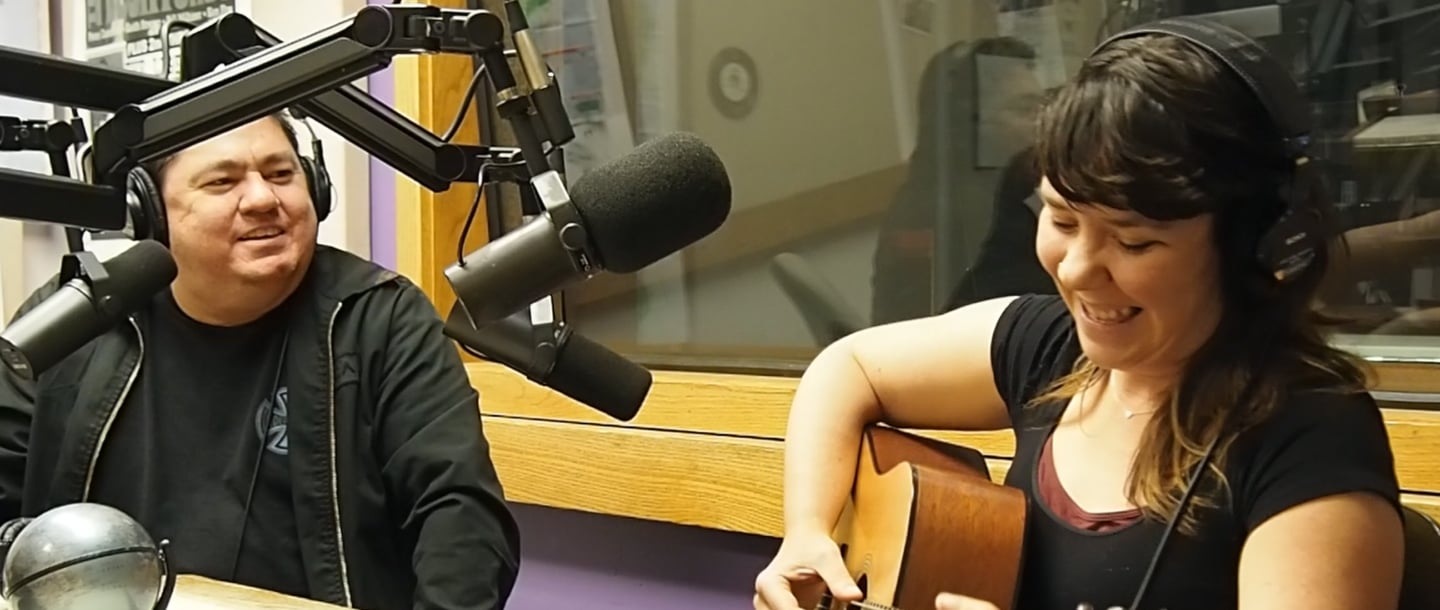Chuck Rodriguez with a woman playing a guitar inside the KMSU Radio station studio