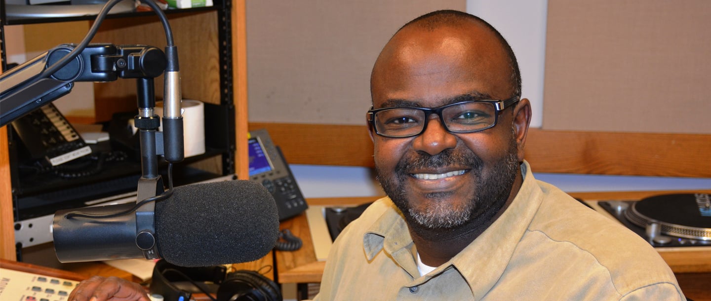 Mohamed Alsadig infront of microphone posing and smiling inside the KMSU Radio station studio