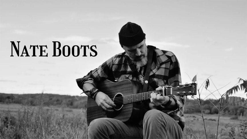 A black and white photo of Nate Boots playing his guitar in a prairie with his name next to him