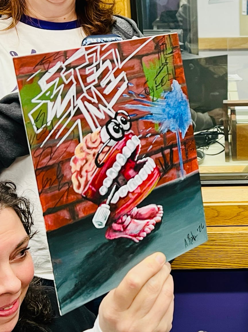 Amber Rahe holding up her painting of brainy teeth in front of graffiti