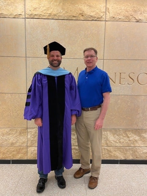 a person standing next to a person in a graduation gown