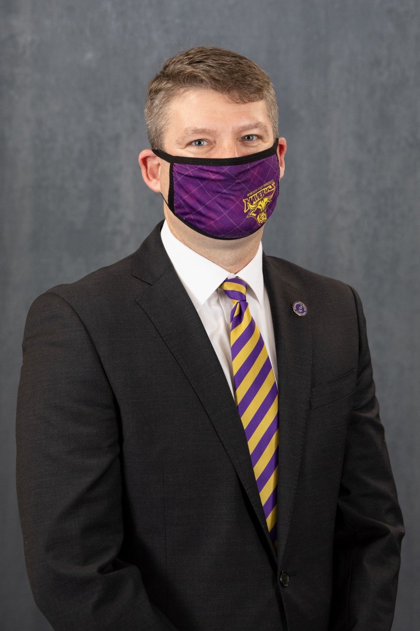 a person in a suit and tie wearing a purple and yellow face mask