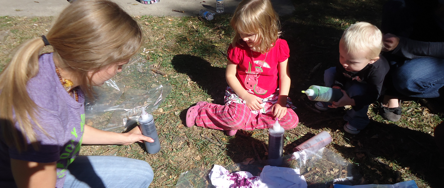 Female student siting on the ground with two children tie dying t-shirts