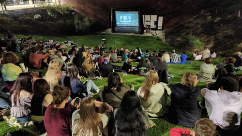 Students watching a movie outside on the campus lawn by the Memorial Library building