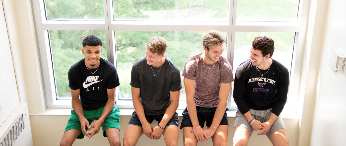 four male students sitting in a window in the hallway of a dorm