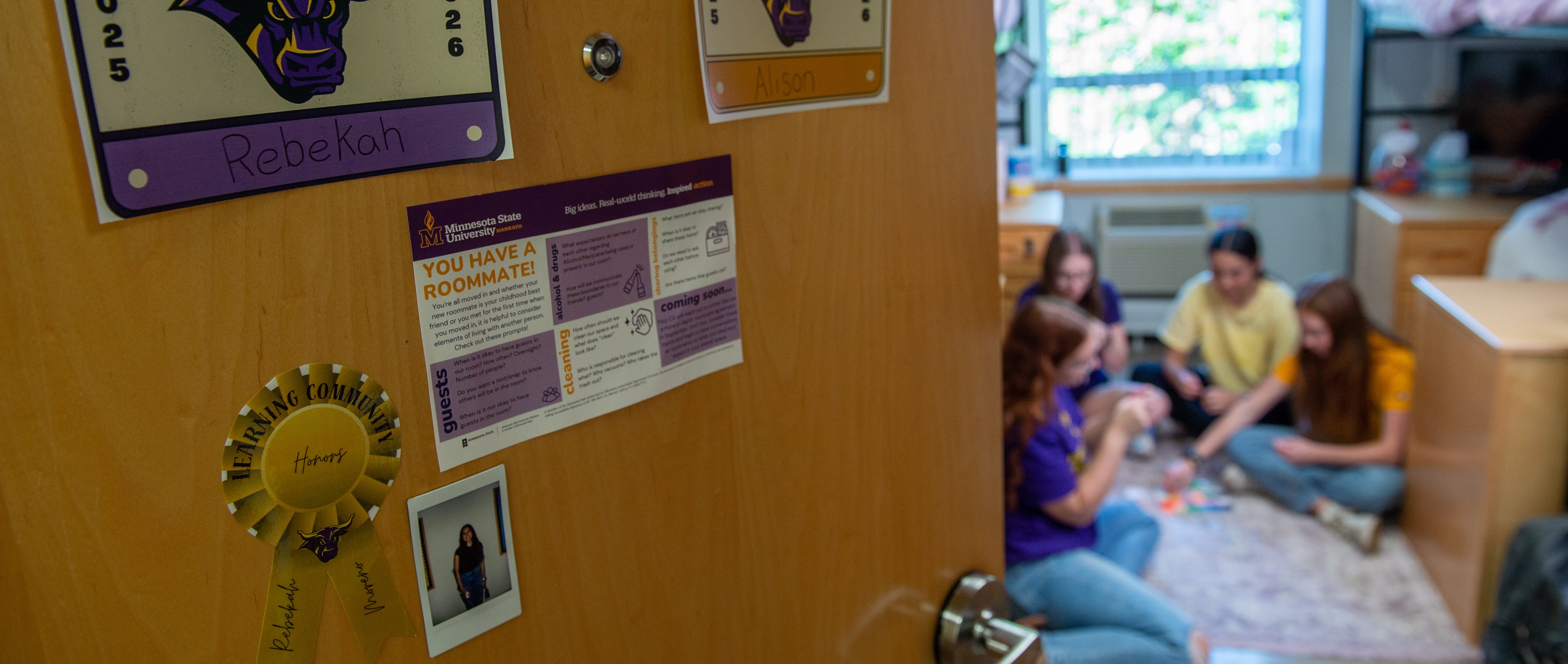 Looking inside an open dorm room door with students socializing on the floor