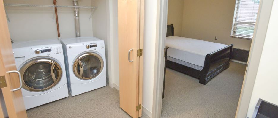 View of utility closet with washer and dryer and bedroom entrance inside the PS 106 Hall Resident staff apartment