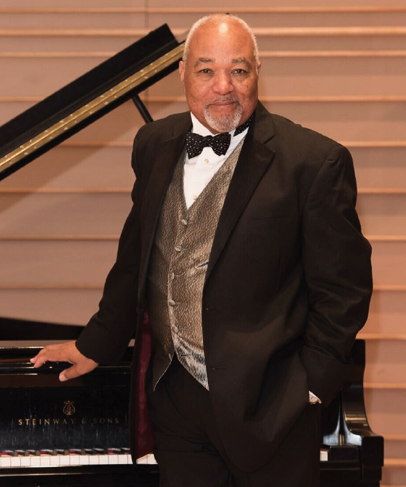a person in a suit and bow tie standing next to a piano